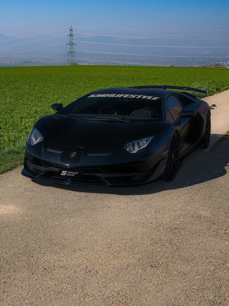 Lamborghini Aventador SVJ en full covering noir vue de face, champ vert et lignes électriques
