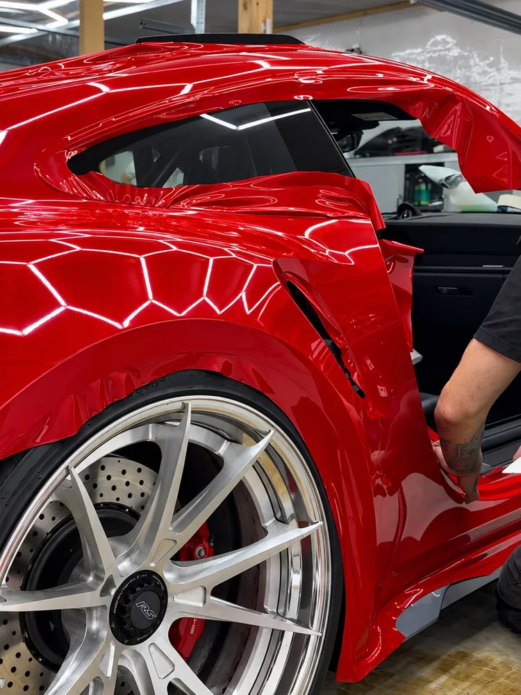 Pose d'un PPF couleur rouge sur l'aile arrière d'une voiture de sport, à l'atelier